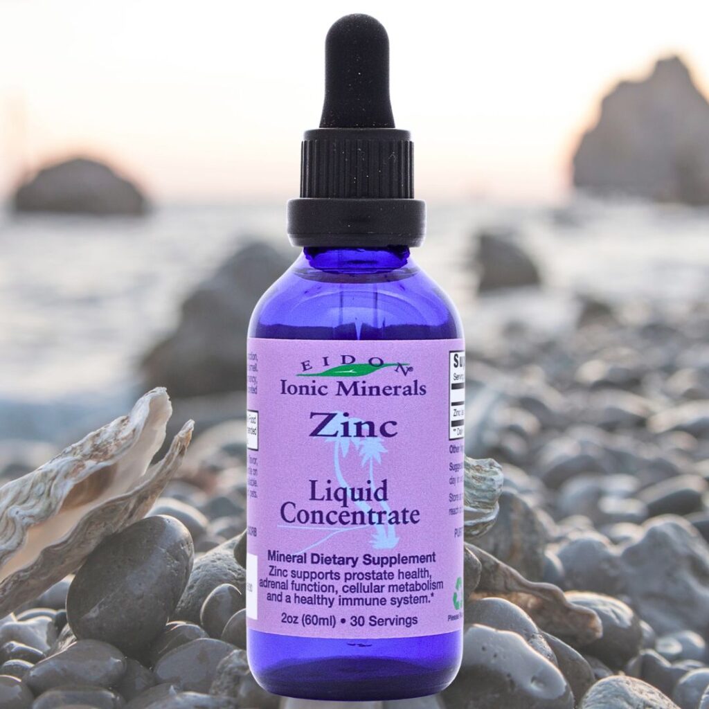 Flaske med Eidon Ionic Minerals flytende mineraltilskudd Sink flytende 60 ml plassert på steinstrand, blå pipetteflaske.